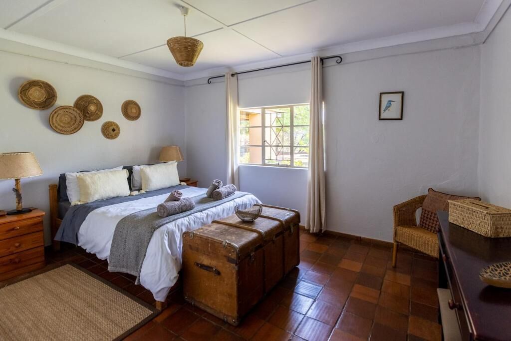 A bedroom with a bed, bedside tables, a window with curtains, and a wicker chair.