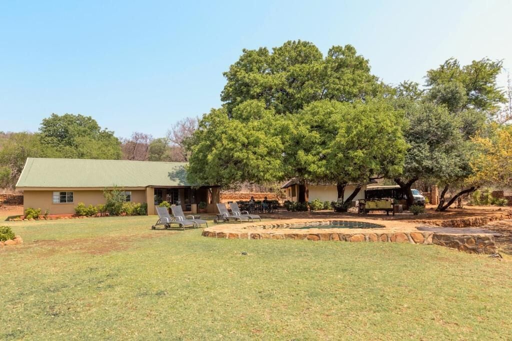 A house with a lawn, a large tree, and a patio area with chairs.