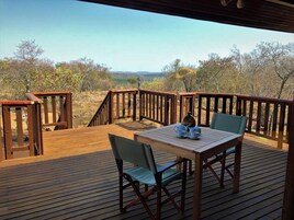 A wooden deck with a table and chairs, overlooking a natural landscape.