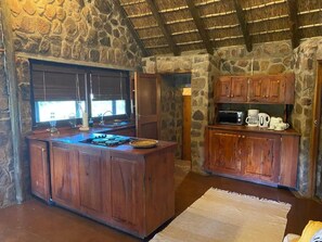 A rustic kitchen with a stone wall, wooden cabinets, and a thatched roof.