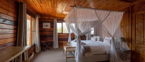 A wooden cabin bedroom with a four-poster bed, a wooden bench, and a window with curtains.