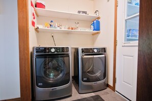 A laundry room with two Maytag front-loading washers and a shelf above containing various items. - Panoramic Views, Sunrise/Sunset, EV Charger Kayaks (Magnetawan)