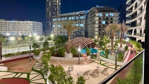 A rooftop pool area with lounge chairs, palm trees, and a distinctive curved building structure. - 48 Parkside - 603 1BD (Dubai)