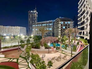 A rooftop pool area with lounge chairs, palm trees, and a distinctive curved building structure. - 48 Parkside - 603 1BD (Dubai)