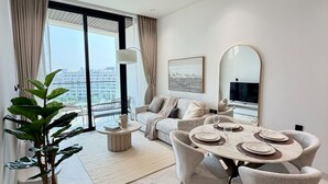 A modern dining area with a round table, chairs, and a view of the city through large windows. - 48 Parkside - 603 1BD (Dubai)