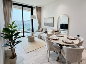 A modern dining area with a round table, chairs, and a view of the city through large windows. - 48 Parkside - 603 1BD (Dubai)