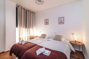 A double bed with two pillows and a folded towel, a bedside table with a lamp, and a window with curtains. - LXR Fuengirola Sun & Beach 2-Bedroom (Fuengirola)