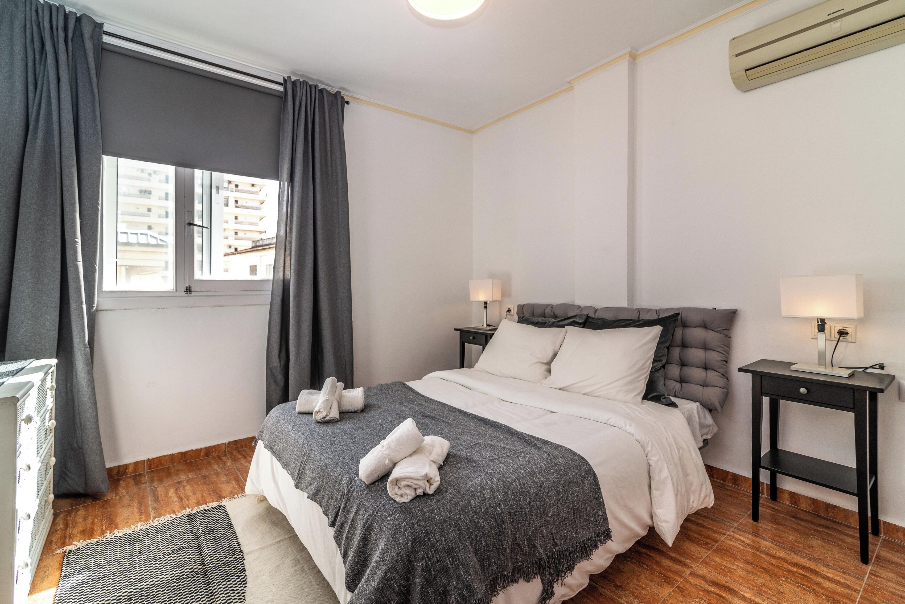 A bedroom with a bed, two bedside tables, a window with curtains, and a radiator.