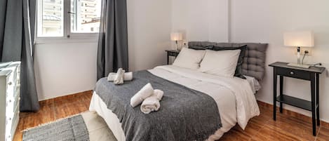 Un dormitorio con cama, dos mesitas de noche, una ventana con cortinas y un radiador.
