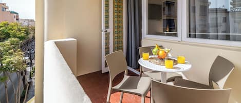 Un balcón con una mesa para dos, sillas y una ventana con cortinas.