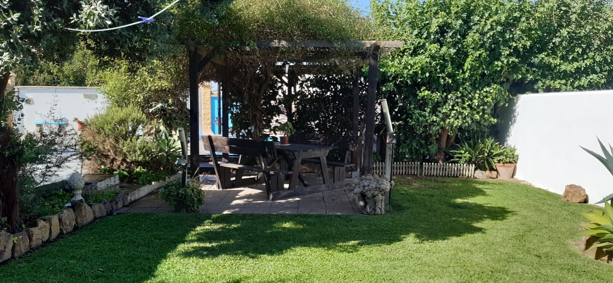 Een tuin met een houten pergola, een tafel en stoelen.