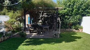Puutarha, jossa on puinen pergola, pöytä ja tuoleja.