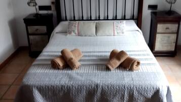 Una cama con una colcha blanca, dos toallas enrolladas y un cabecero con diseño decorativo.
