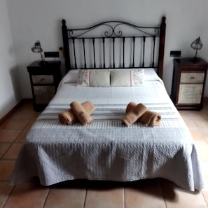 Un llit amb estovatge blanc, dues tovalloles enrotllades i un capçal decoratiu.