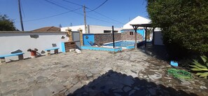 Un patio de piedra con piscina, un espacio de estar cubierto y un muro blanco con detalles azules.