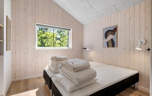 A bedroom with a bed, a window, a wall-mounted lamp, and a painting.