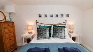 A bedroom with a bed, two nightstands, a dresser, and a wall with framed pictures. - Cobblers Cottage (Reydon)