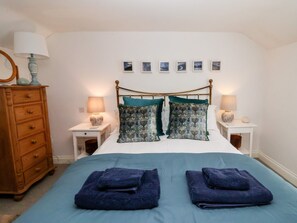 A bedroom with a bed, two nightstands, a dresser, and a wall with framed pictures. - Cobblers Cottage (Reydon)