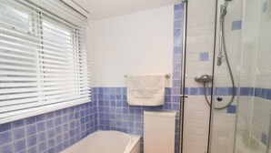A bathroom with a bathtub, a shower, and a window with blinds. - Cobblers Cottage (Reydon)