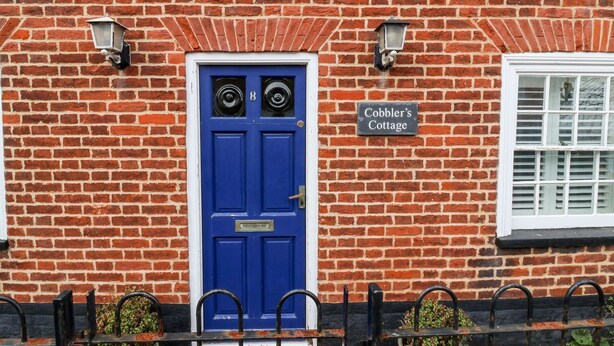 A red brick building with a blue door, a sign reading 'Cobbler's Cottage,' and a window with shutters. - Cobblers Cottage (Reydon)