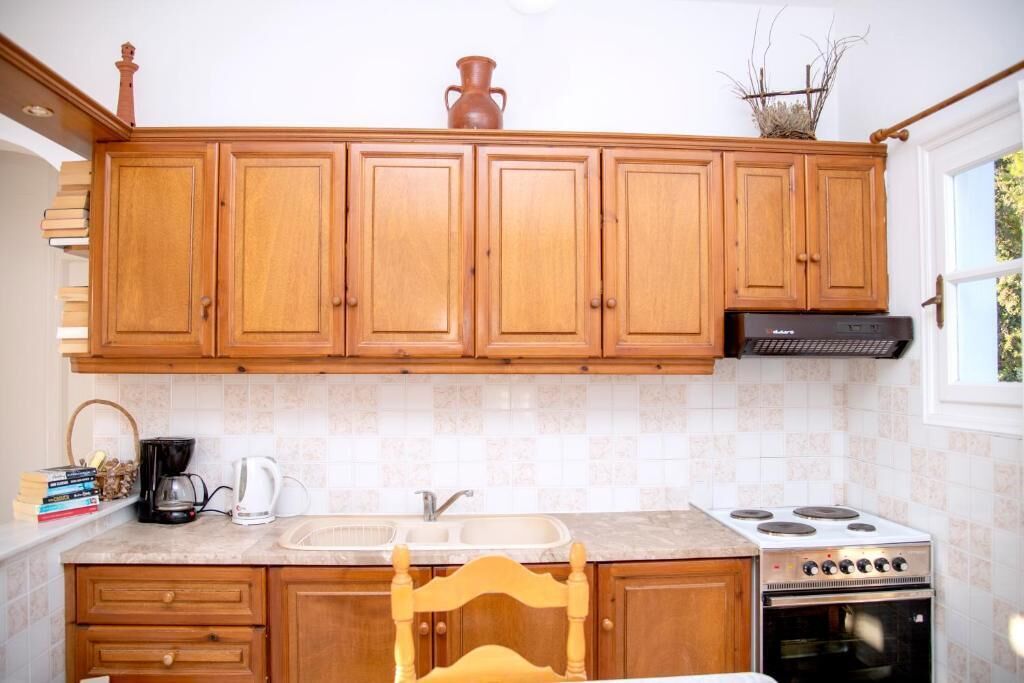 A kitchen with wooden cabinets, a stove, a sink, and a chair.