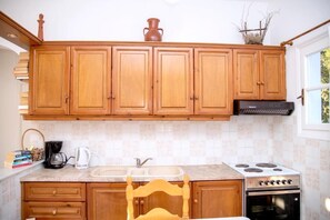 A kitchen with wooden cabinets, a stove, a sink, and a chair. - Argo Studios (Kini)