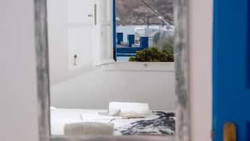 Un miroir reflétant une pièce avec un lit, une porte bleue et une vue sur un bâtiment aux structures blanches et bleues.
