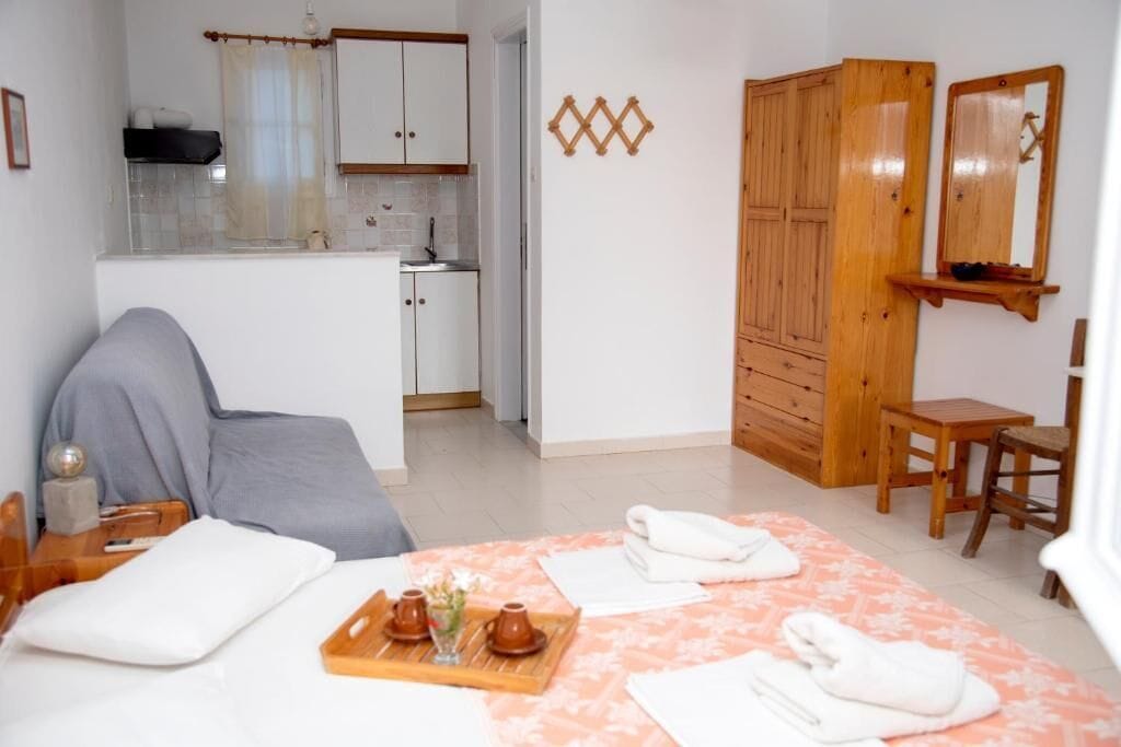 Une chambre comprenant un lit, une petite table avec des serviettes, une armoire en bois et un coin cuisine.