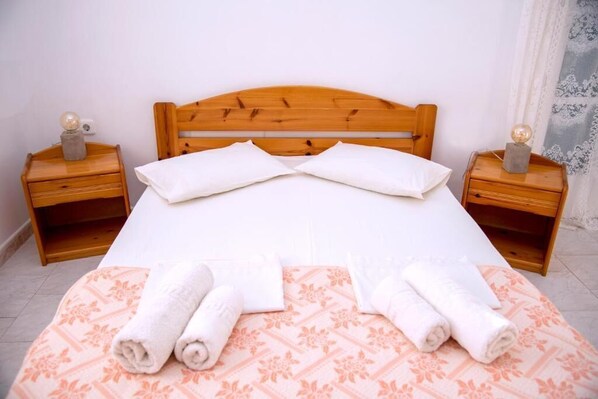 A neatly made bed with white linens and pillows, two wooden nightstands with lamps, and a patterned bedspread.
