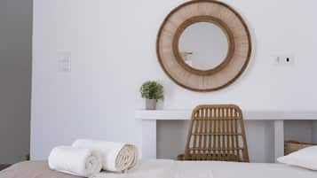 Une pièce comprenant un lit, un miroir rond, une chaise en osier et une petite plante en pot.