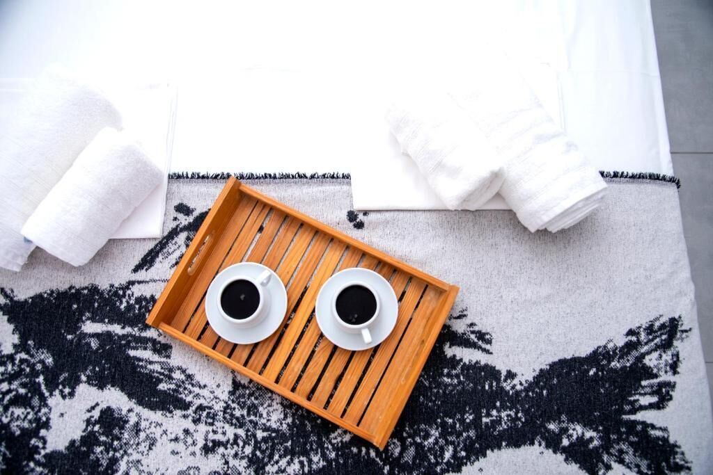 Un plateau en bois sur lequel reposent deux tasses de café, le tout posé sur un tapis à motifs.