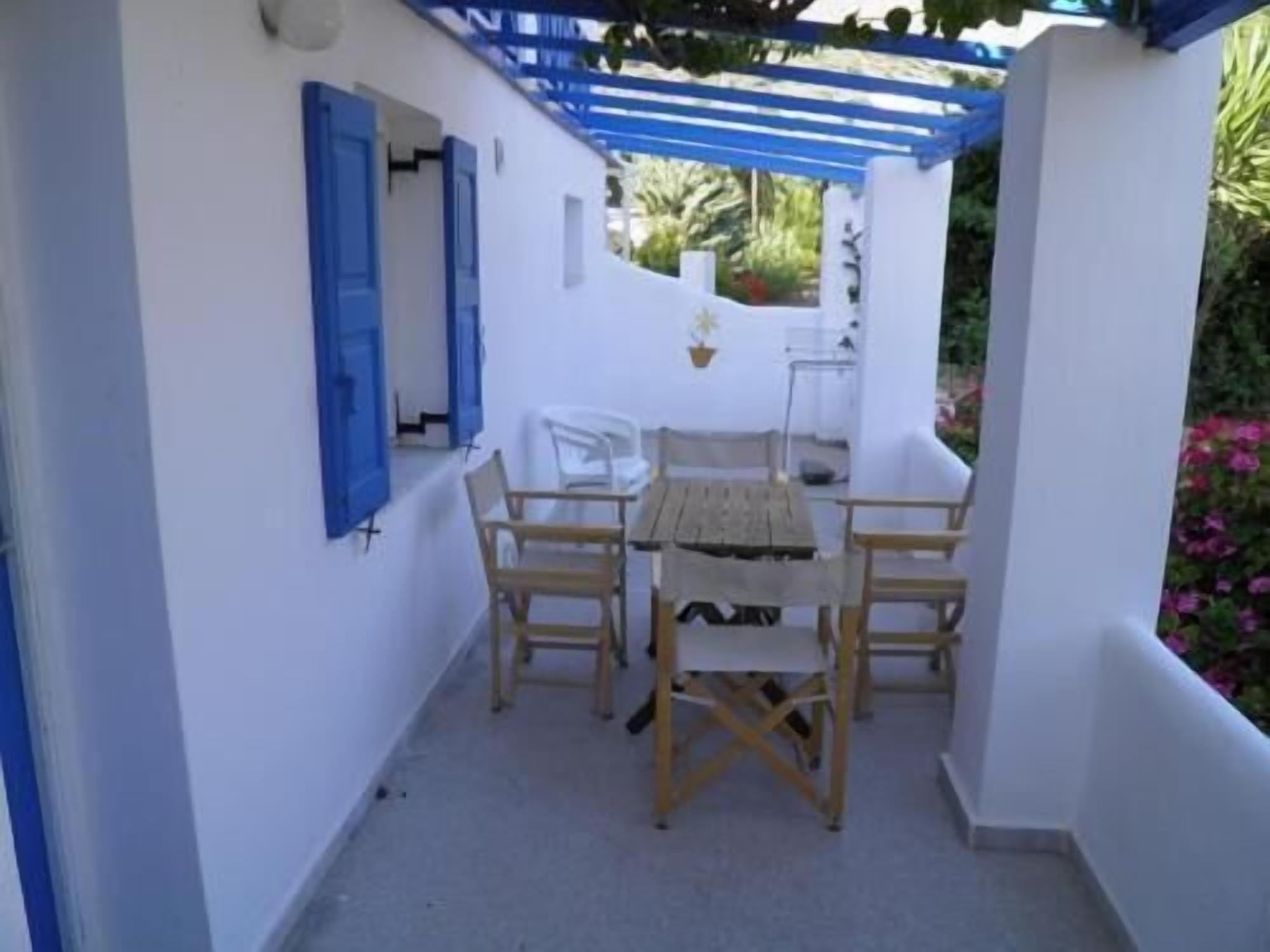 A covered outdoor seating area with a table and chairs, a white wall, and a blue awning.