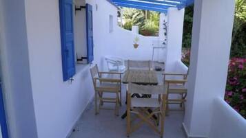 Un espacio de estar al aire libre cubierto con una mesa, sillas, una pared blanca y un toldo azul.