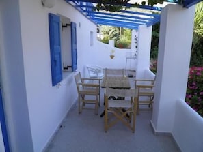 A covered outdoor seating area with a table and chairs, a white wall, and a blue awning. - Argo Studios (Kini)