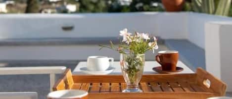 Una mesa con un florero, dos tazas y una bandeja en una terraza con vistas a casas y un cactus al fondo.