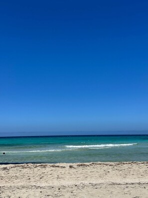 Una playa con cielo azul despejado y mar tranquilo.