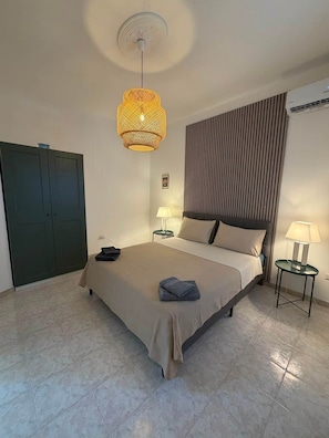Habitación de hotel con una cama grande, dos mesitas de noche con lámparas, un armario oscuro, una lámpara en el techo y un aire acondicionado de pared.