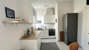 A modern kitchen with white cabinets, a stainless steel trash bin, a wicker chair, and a refrigerator. - Matino Terrace with Ocean View (Matino)