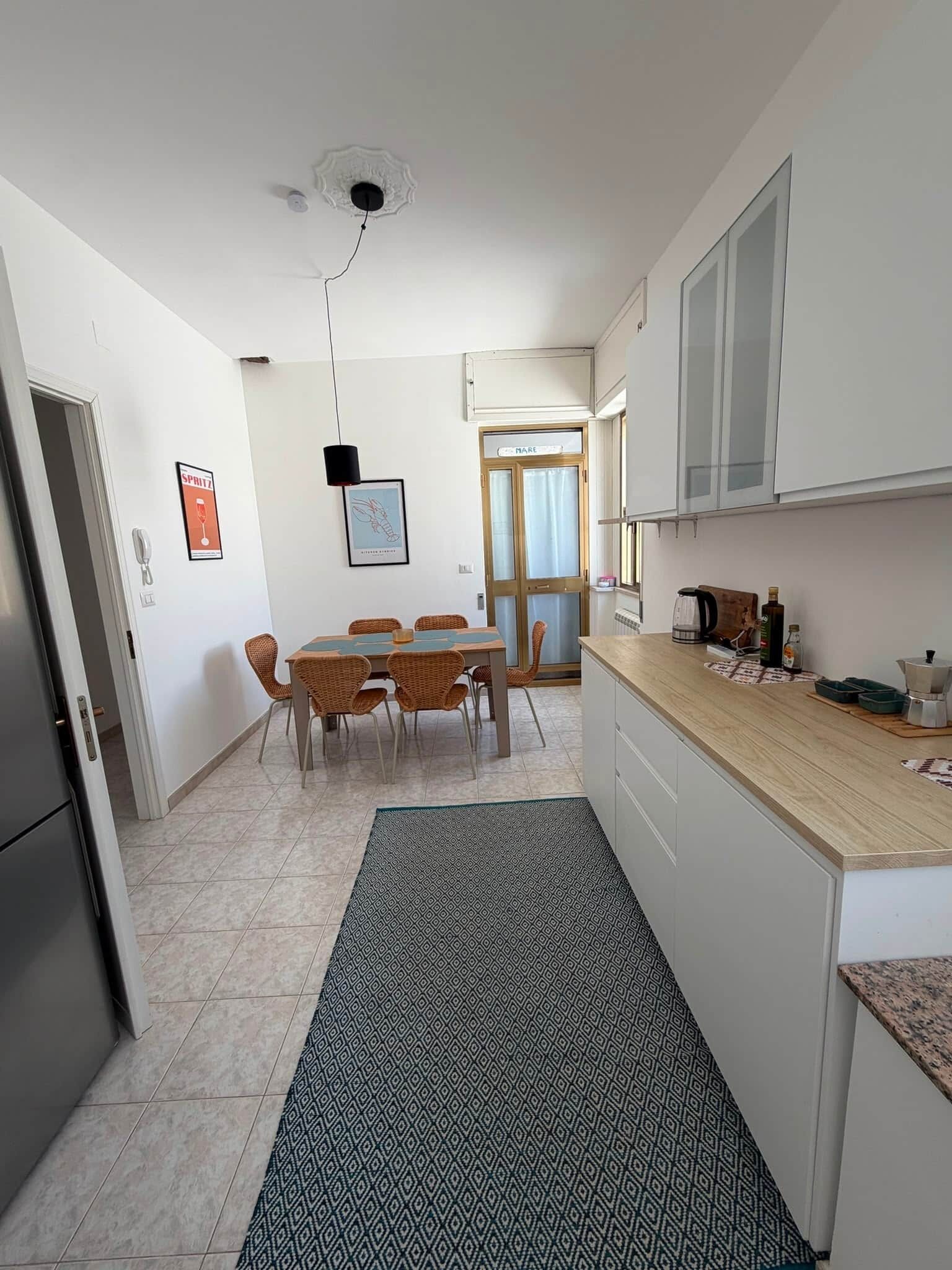 A compact kitchen with a dining area, a refrigerator, a coffee machine, and a patterned rug.