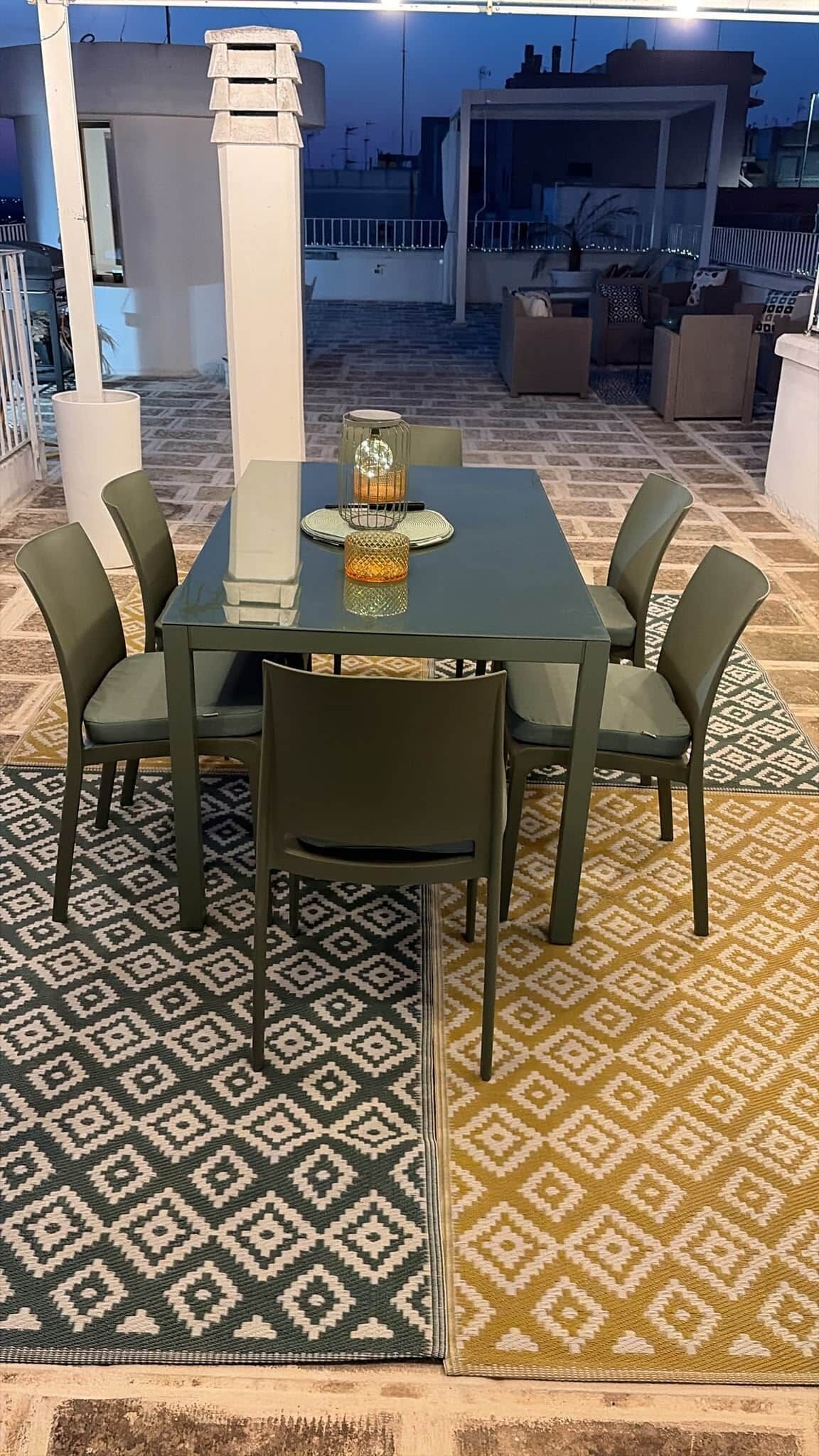 An outdoor patio with a table and chairs, patterned rugs, and a view of the surrounding area.