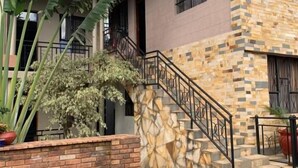 A two-story building with a staircase, potted plants, and a brick wall. - Peakline Apartments (Arusha)