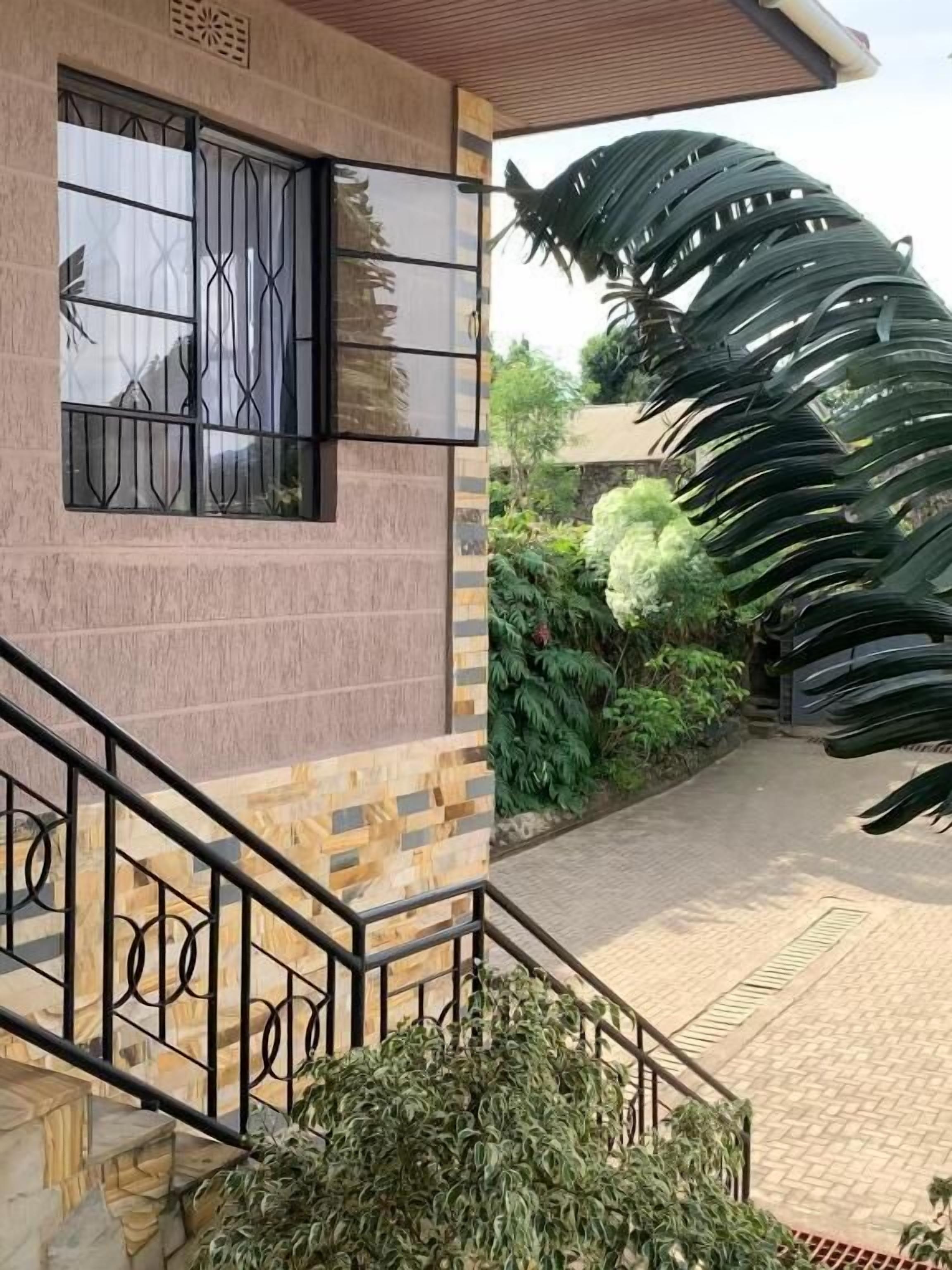 A building with a staircase, a window with metal bars, and a large green plant.