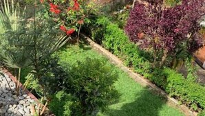 A garden with a paved walkway, a seating area with a table and chairs, and various plants and shrubs. - Peakline Apartments (Arusha)