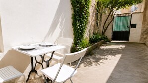 Eine kleine Terrasse im Freien mit Tisch und Stühlen, umgeben von einer niedrigen Mauer und Topfpflanzen.