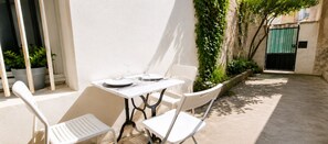 Eine kleine Terrasse im Freien mit Tisch und Stühlen, umgeben von einer niedrigen Mauer und Topfpflanzen.