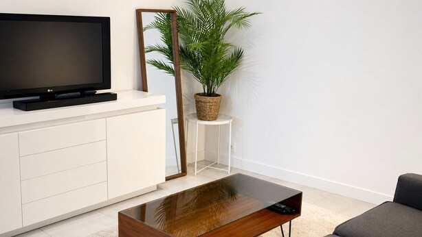 Uma sala de estar moderna com televisão de tela plana, uma mesa de centro de madeira, um vaso com planta e um sofá cinza.