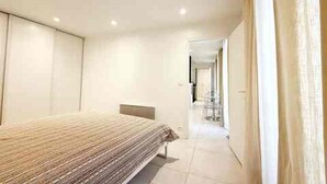 Quarto de hotel moderno com uma cama, uma mesinha e vista para o corredor.