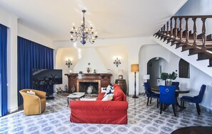 Ein Wohnzimmer mit Kamin, einem roten Sofa, einer Kristallleuchtre und einer Treppe.