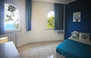 Une pièce avec deux fenêtres, un lit, une table de chevet et une lampe.