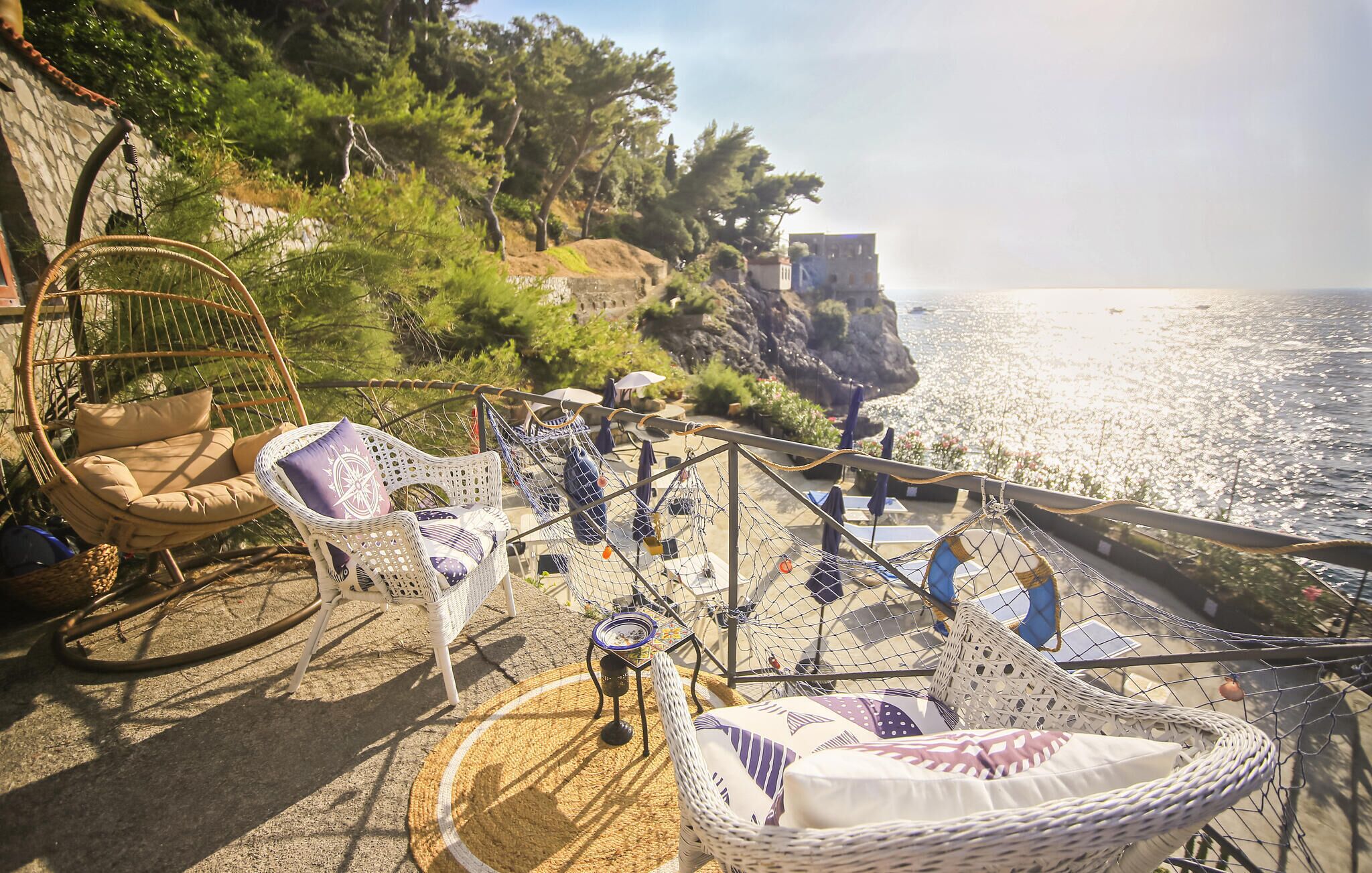 Eine Küsten-Terrasse mit Korbmöbeln, einer Seilschaukel und Blick auf das Meer.
